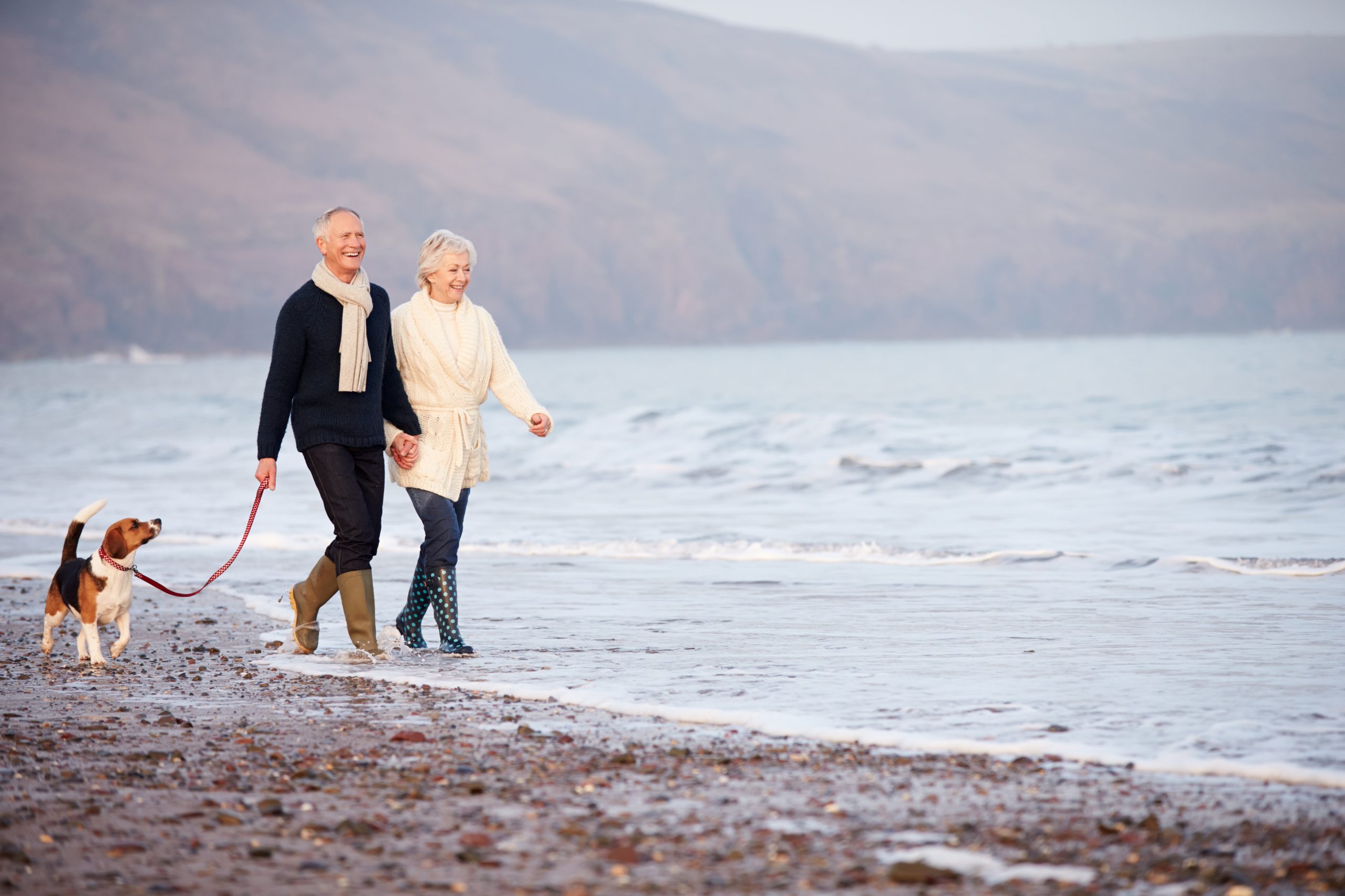 Senior Couple Walking Along Winter Beach With Pet Dog Smiling